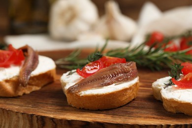 Photo of Delicious sandwiches with cream cheese, anchovies and tomatoes on wooden board, closeup