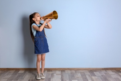 Photo of Cute little girl with megaphone near color wall