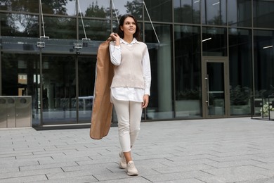 Photo of Attractive happy woman holding garment cover with clothes outdoors. Dry cleaning service