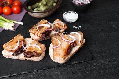 Photo of Tasty fried pork lard with bread slices and onion on black table