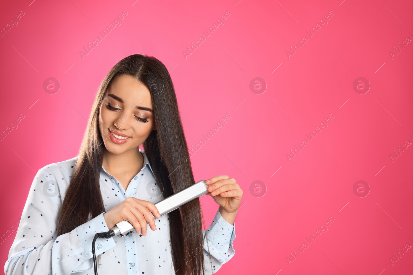 Photo of Happy woman using hair iron on color background. Space for text