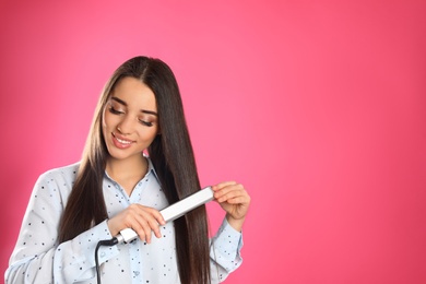 Happy woman using hair iron on color background. Space for text