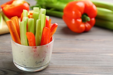 Photo of Celery and other vegetable sticks with dip sauce in glass bowl on wooden table. Space for text