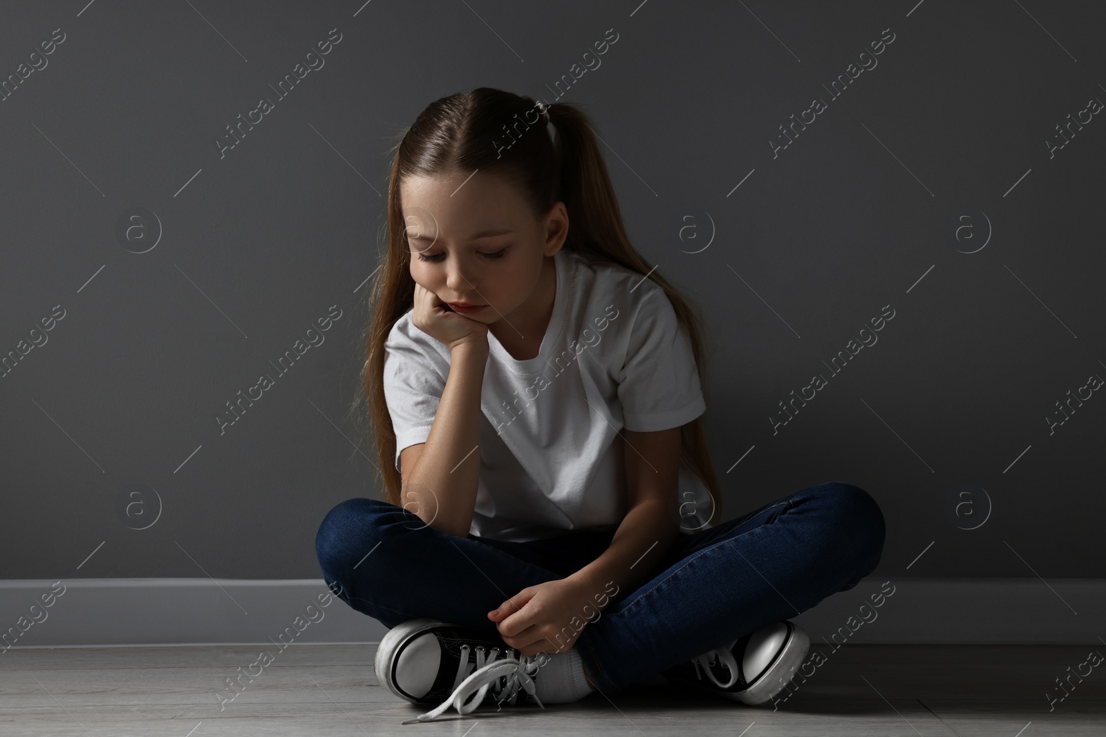 Photo of Sad girl sitting on floor near dark grey wall indoors