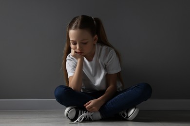 Sad girl sitting on floor near dark grey wall indoors