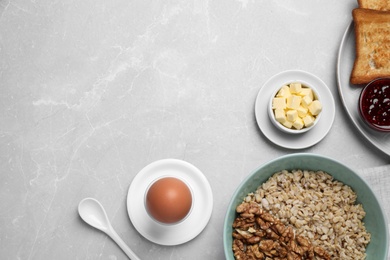 Photo of Tasty breakfast with oatmeal porridge, egg and toasts on light grey marble table, flat lay. Space for text