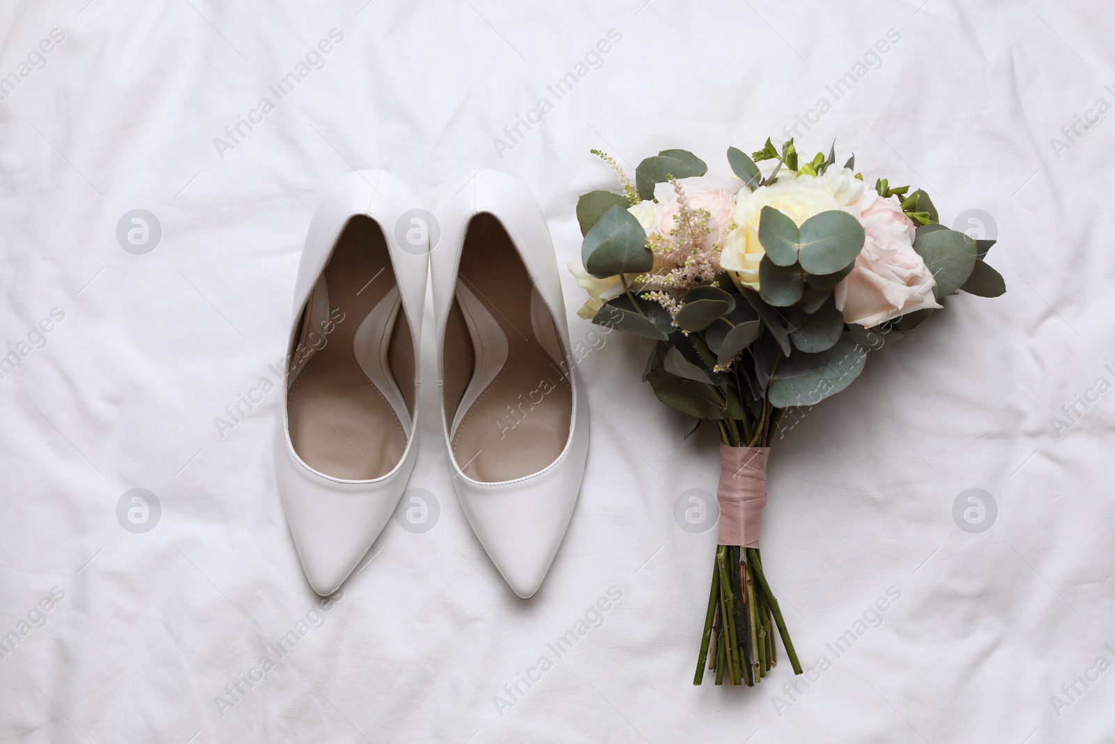 Photo of Pair of wedding high heel shoes and beautiful bouquet on white fabric, flat lay