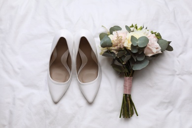 Photo of Pair of wedding high heel shoes and beautiful bouquet on white fabric, flat lay