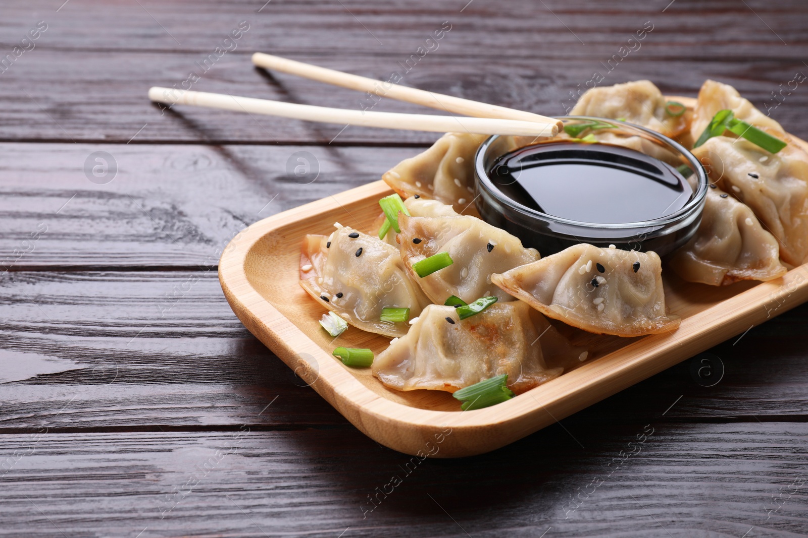 Photo of Delicious gyoza (asian dumplings) with green onions, soy sauce and chopsticks on wooden table. Space for text
