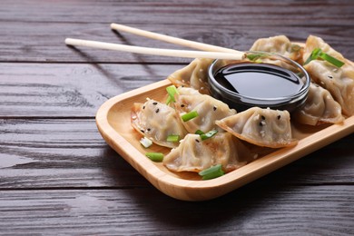 Photo of Delicious gyoza (asian dumplings) with green onions, soy sauce and chopsticks on wooden table. Space for text
