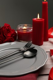 Photo of Romantic place setting with red candles and roses on wooden table, closeup. St. Valentine's day dinner