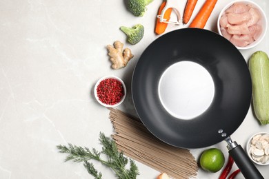 Photo of Empty iron wok surrounded by raw ingredients on light table, flat lay. Space for text