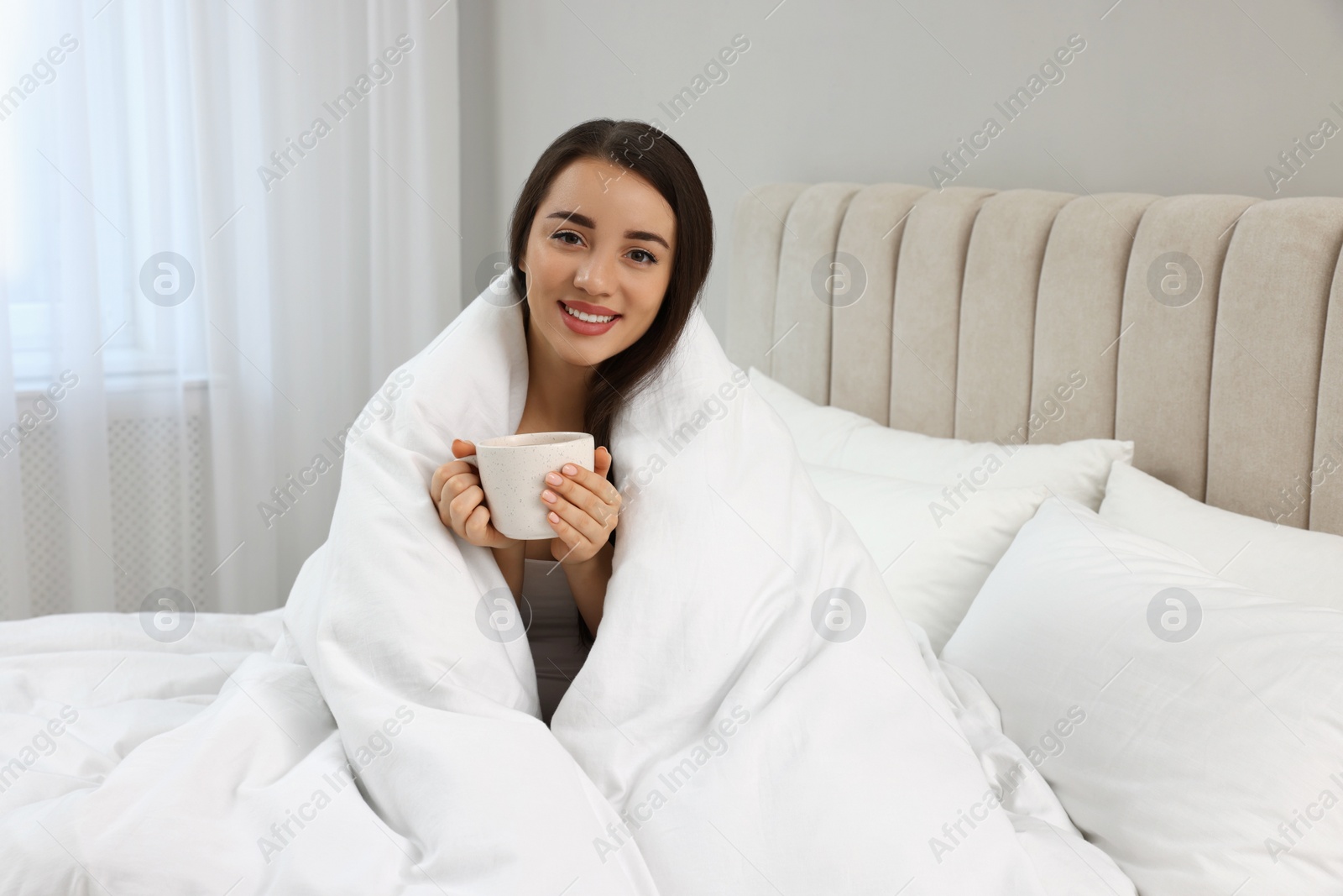 Photo of Beautiful young woman with cup of drink wrapped in blanket at home