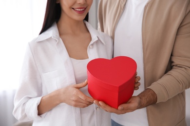 Photo of Lovely couple with gift box at home, closeup. Valentine's day celebration
