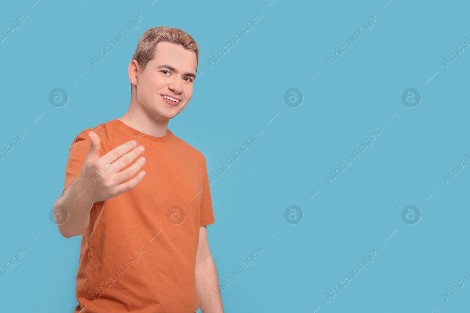 Photo of Happy man inviting to come in against light blue background, space for text