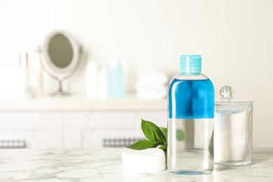 Photo of Cotton pads, leaves and makeup removal product on white marble table in bathroom. Space for text