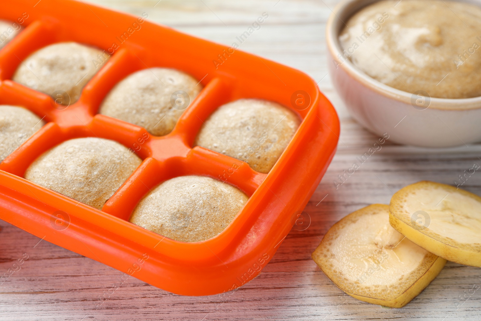 Photo of Banana puree in ice cube tray with ingredients on white wooden table, closeup