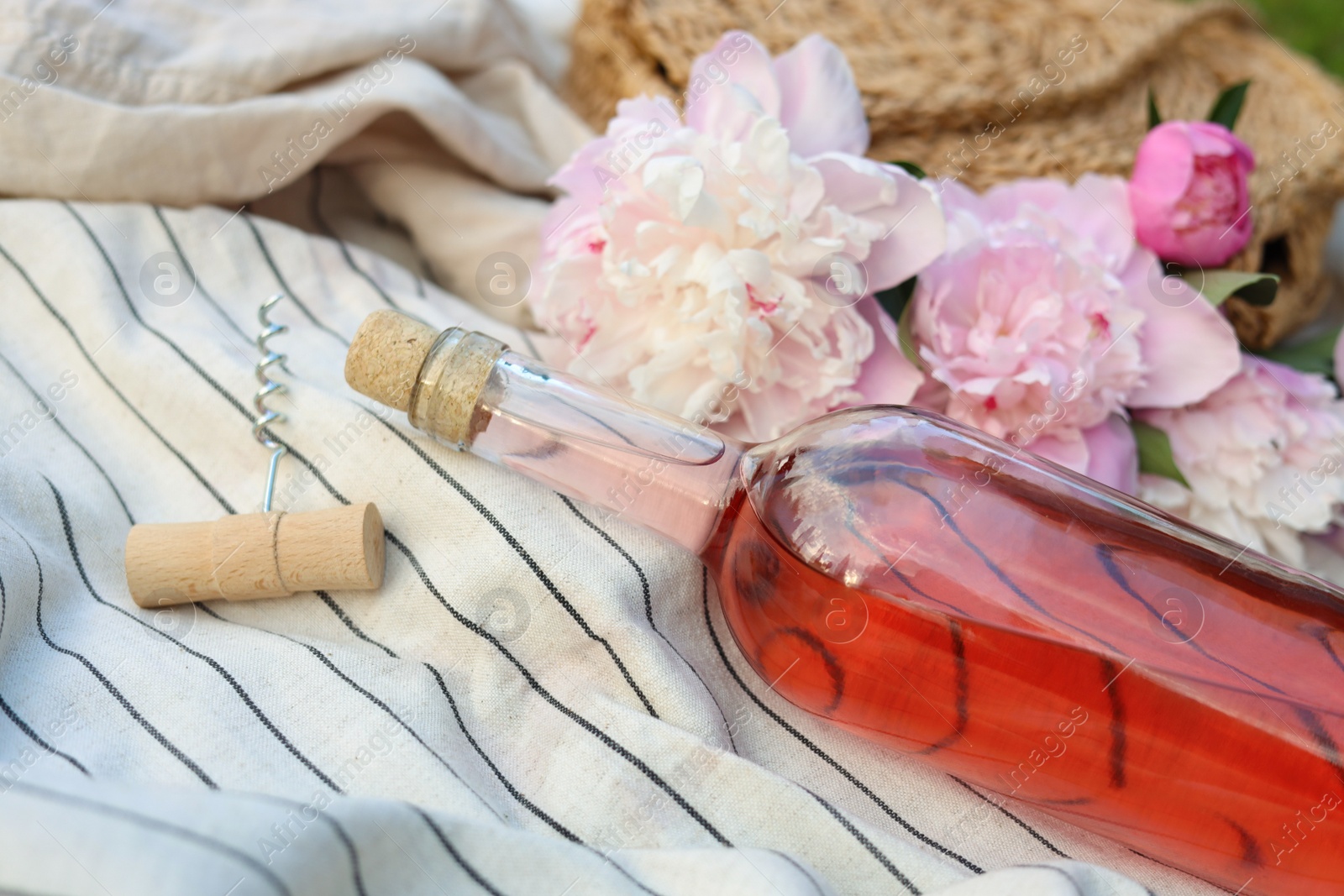 Photo of Bottle of rose wine and beautiful peonies on light blanket, closeup