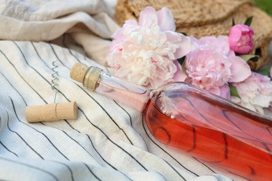 Photo of Bottle of rose wine and beautiful peonies on light blanket, closeup