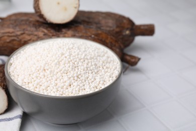 Tapioca pearls in bowl and cassava roots on white tiled table, closeup