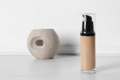 Photo of Bottle of skin foundation on white floor, space for text. Makeup product