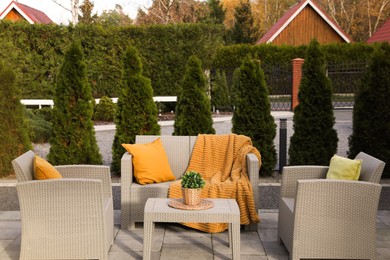 Photo of Beautiful rattan garden furniture, soft pillows, blanket and houseplant in backyard