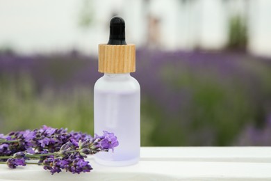 Bottle of essential oil and lavender flowers on white wooden table in field