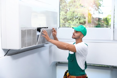 Professional technician maintaining modern air conditioner indoors