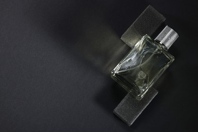 Photo of Stylish presentation of luxury men`s perfume in bottle on black background, top view. Space for text