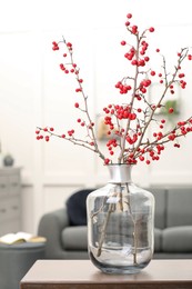 Photo of Hawthorn branches with red berries on table in living room