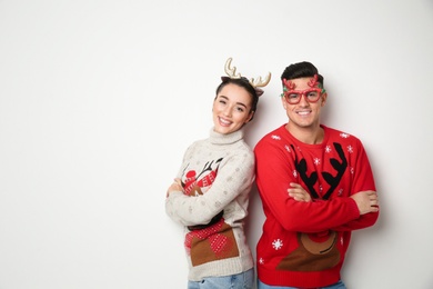 Photo of Couple in Christmas sweaters, deer headband and party glasses on white background, space for text