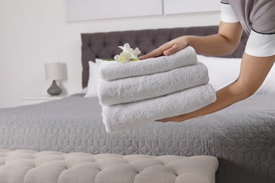 Maid holding fresh towels with flowers in hotel room, closeup