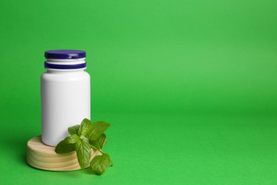 Photo of Plastic medicine bottle and leaves on green background, space for text. Medicament