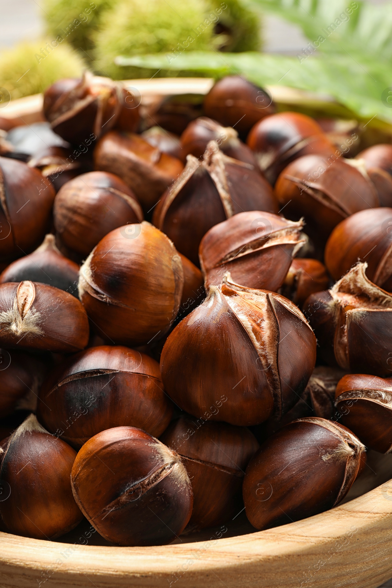Photo of Delicious roasted edible chestnuts in wooden bowl, closeup