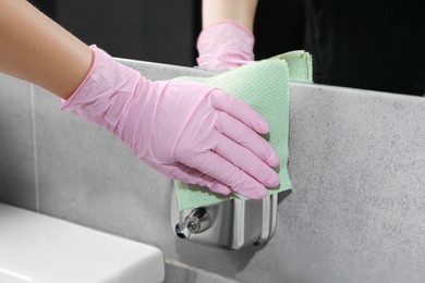 Photo of Woman in glove cleaning liquid soap dispenser with paper towel, closeup