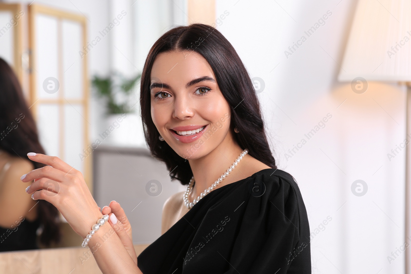 Photo of Young woman trying on elegant pearl bracelet indoors