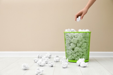 Photo of Woman throwing crumpled paper into metal bin against color wall. Space for text