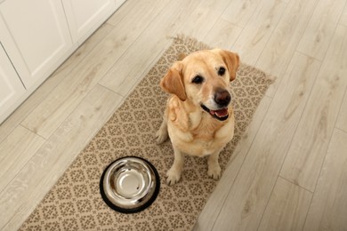 Photo of Cute Labrador Retriever waiting near feeding bowl on floor indoors, above view