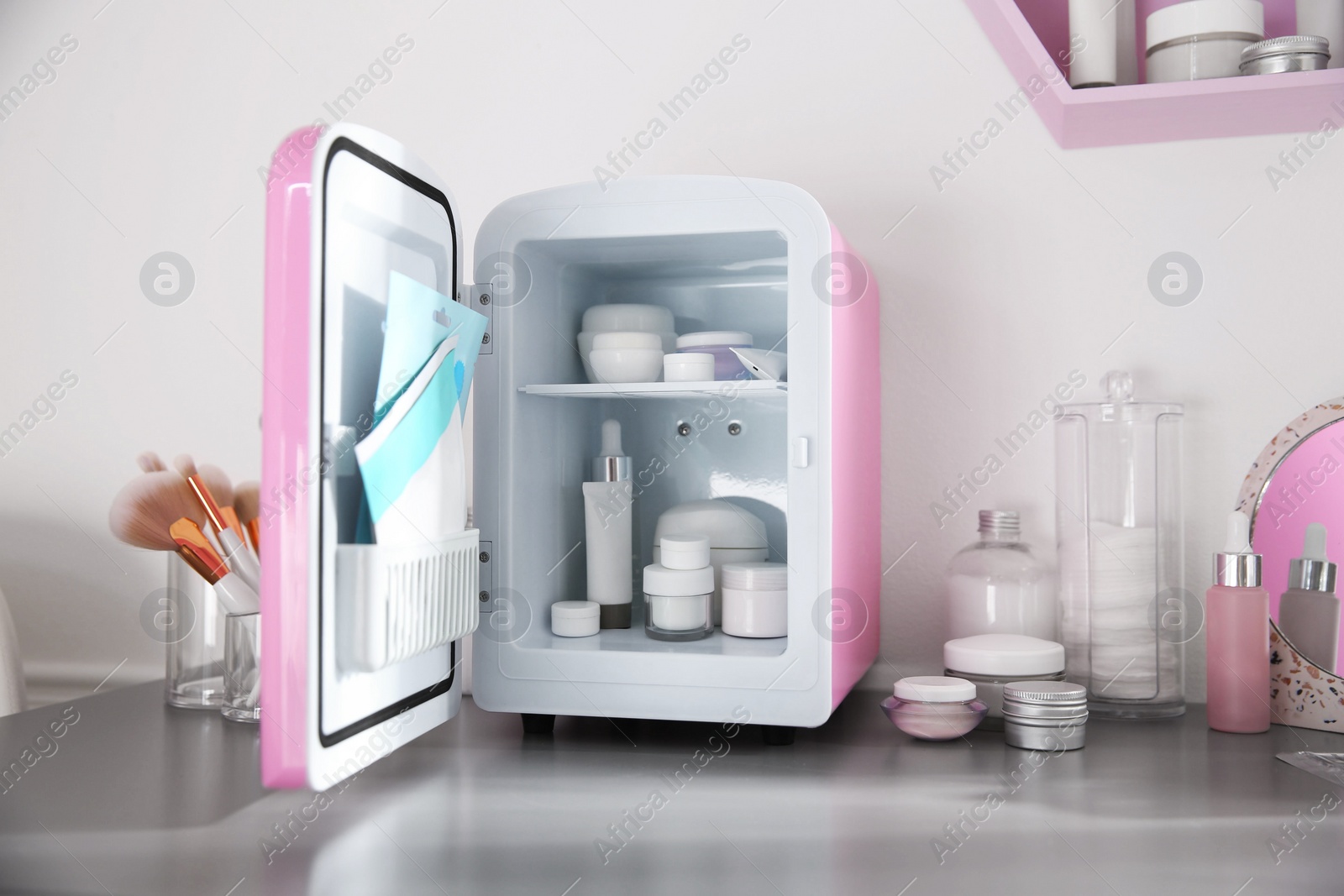 Photo of Mini fridge with cosmetic products on grey vanity table indoors