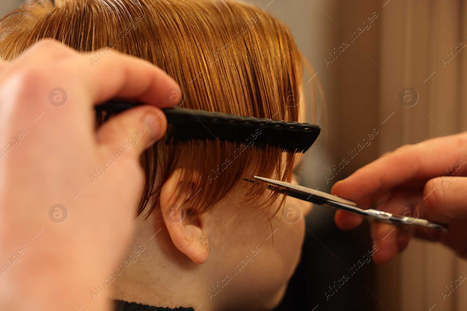 Photo of Professional hairdresser cutting boy's hair in beauty salon, closeup