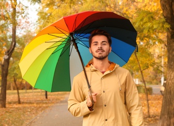 Photo of Young man with bright umbrella walking in park