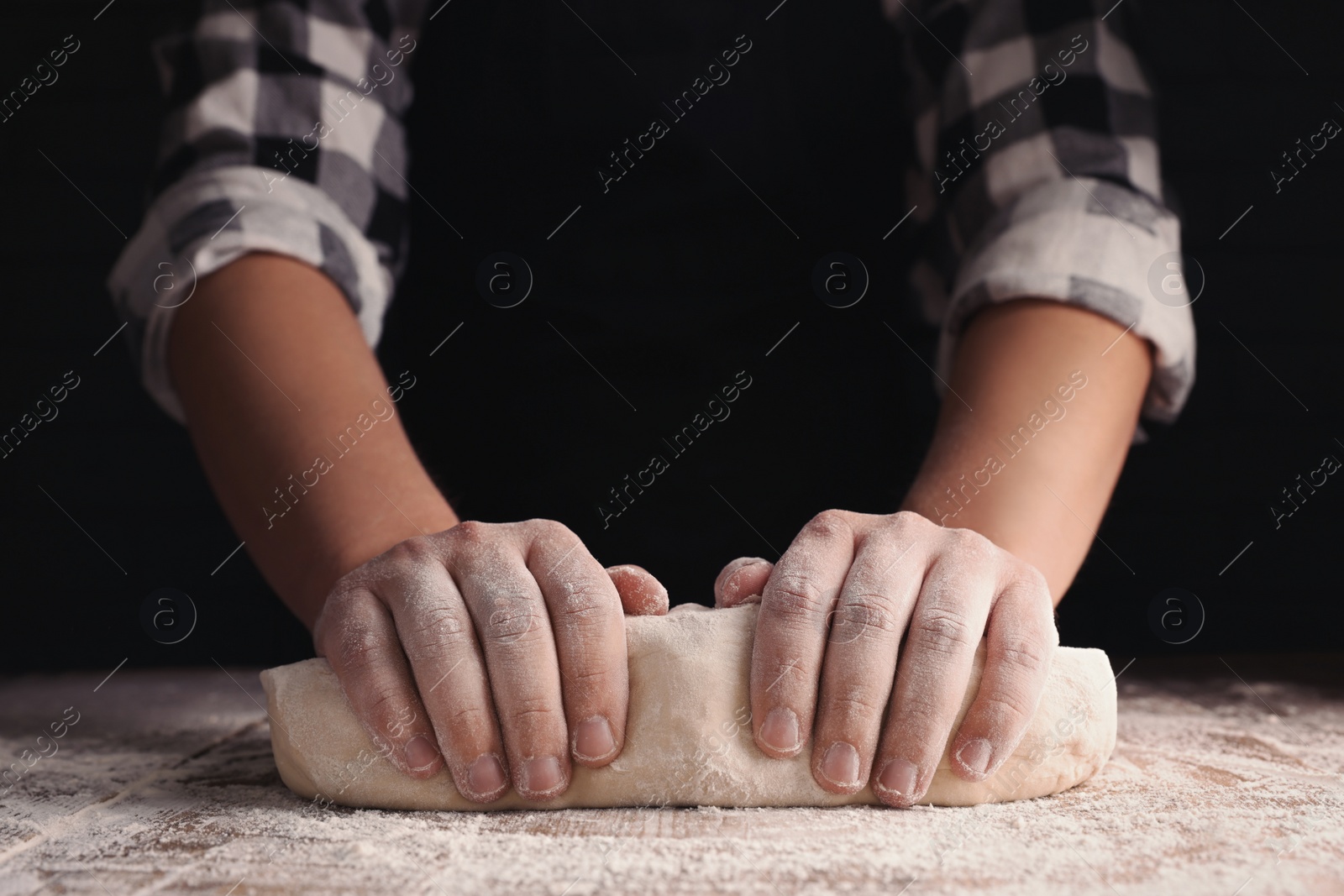 Photo of Man kneading dough at wooden table on dark background, closeup