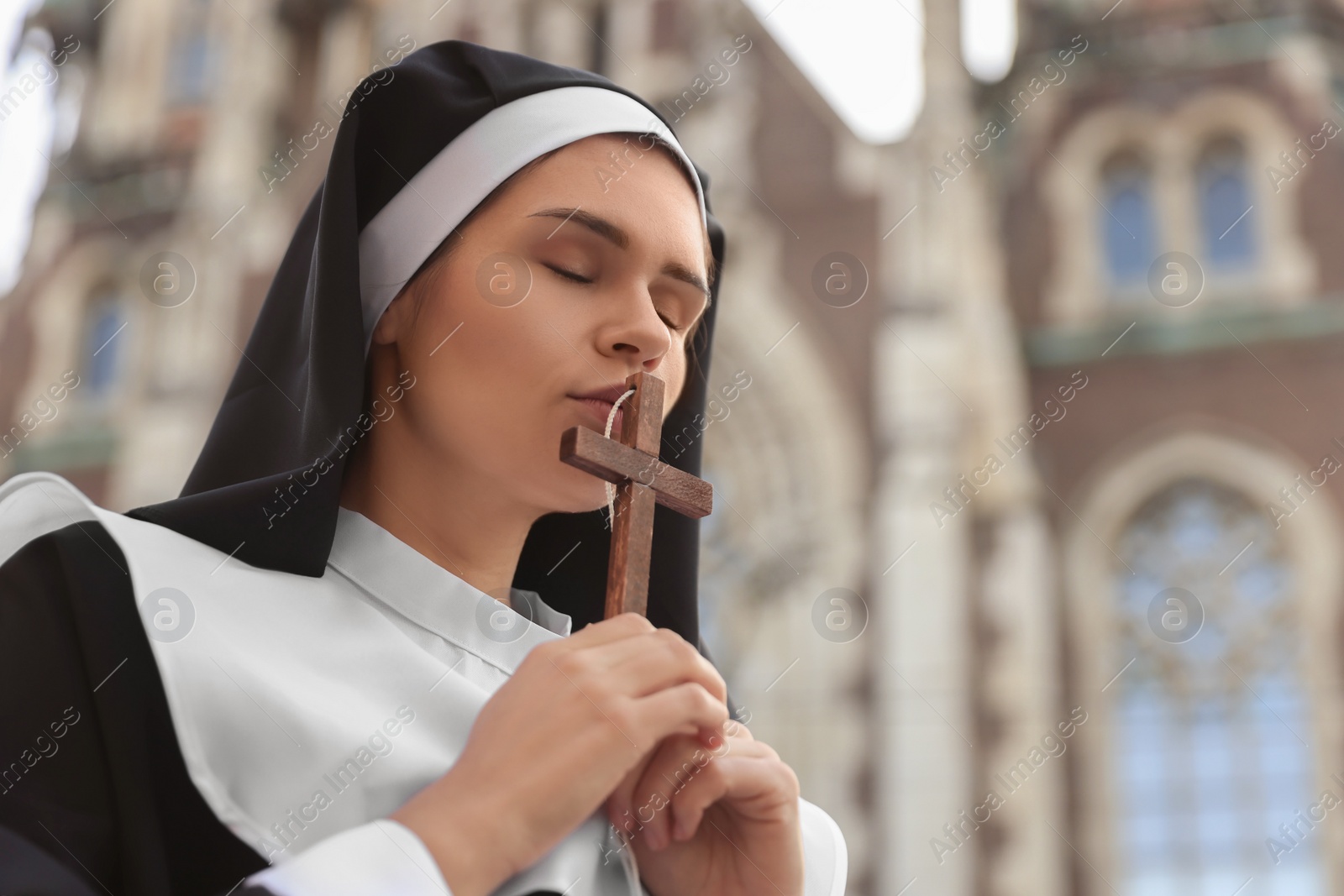 Photo of Young nun with Christian cross near cathedral outdoors, space for text