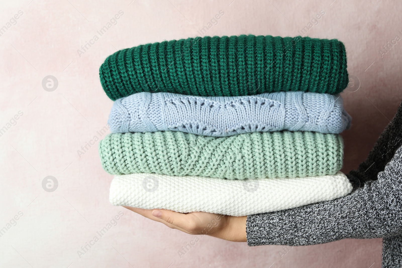 Photo of Woman holding stack of warm clothes on light background, closeup. Autumn season