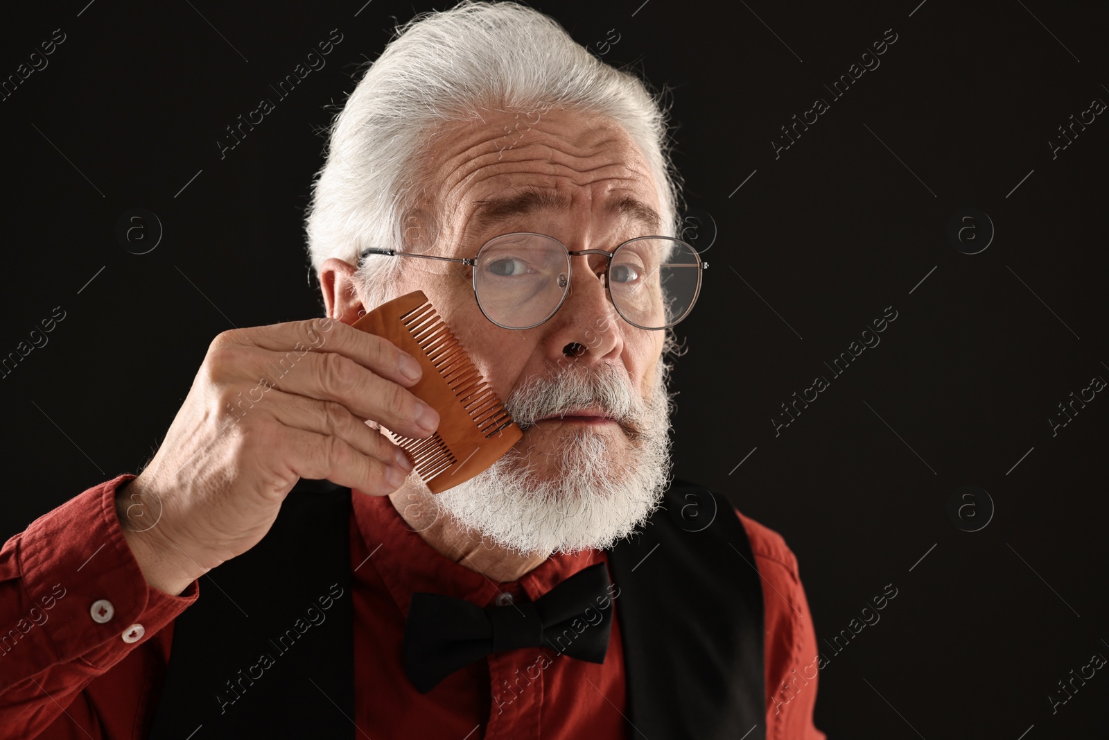 Photo of Senior man combing mustache on black background, space for text