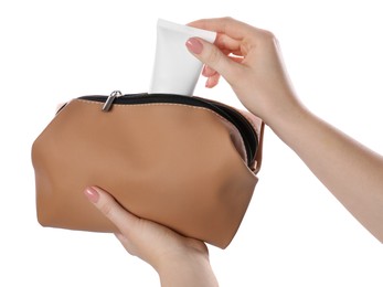 Photo of Woman putting tube of makeup product into cosmetic bag on white background, closeup