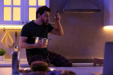 Photo of Man eating soup in kitchen at night. Bad habit