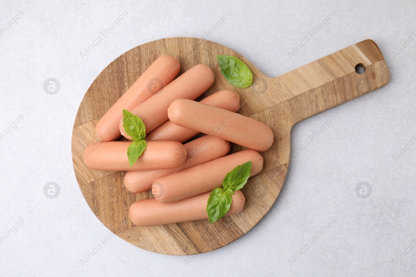 Photo of Delicious boiled sausages and basil on light gray table, top view