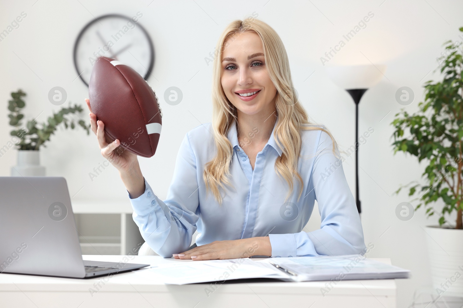 Photo of Happy woman with american football ball at table in office