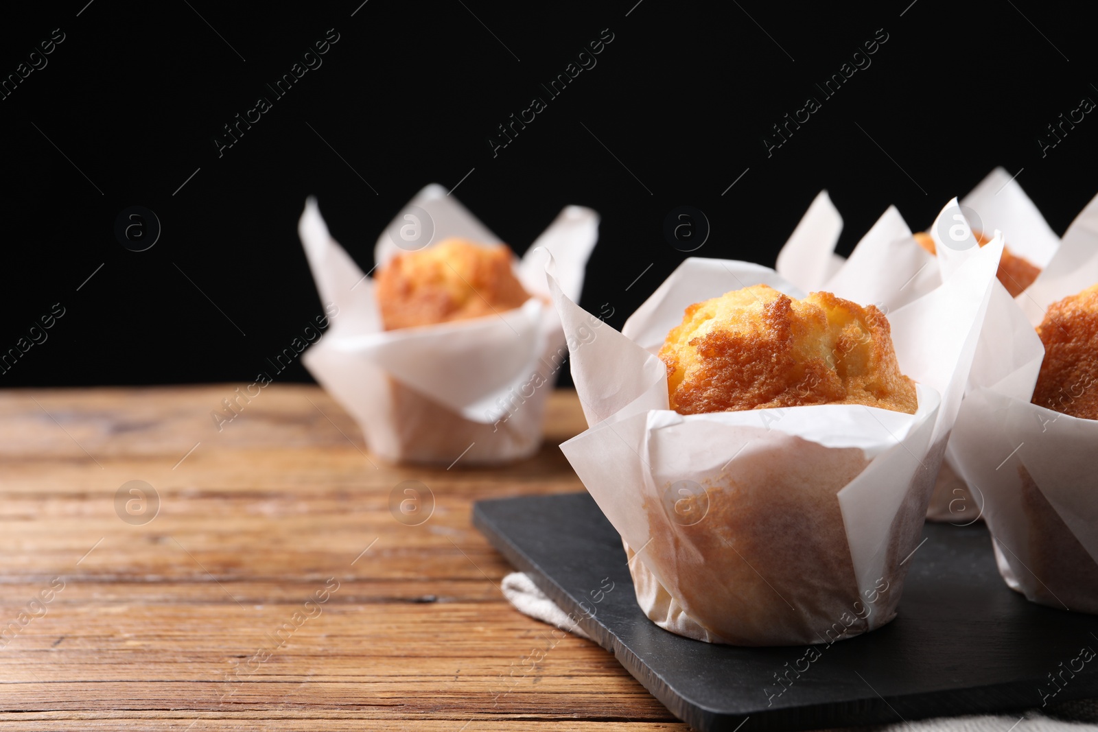 Photo of Delicious sweet muffins on wooden table against dark background, closeup. Space for text